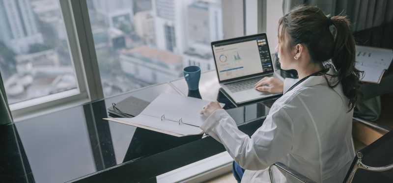 Person in a lab coat is typing on a laptop.