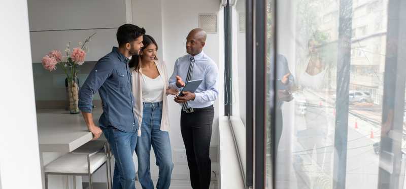 Real estate agent talking to a couple and showing them a property on a tablet computer.