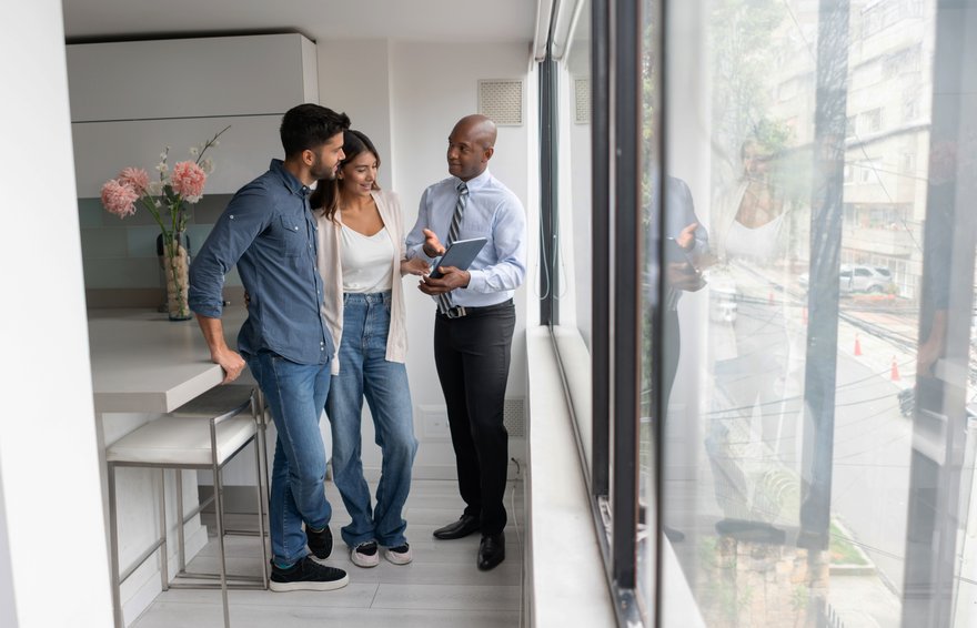 Real estate agent talking to a couple and showing them a property on a tablet computer.