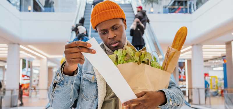 Mall shopper looking at receipt and holding grocery bag.