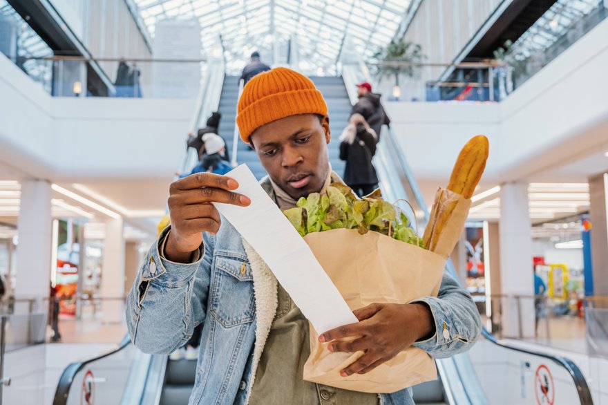 Mall shopper looking at receipt and holding grocery bag.