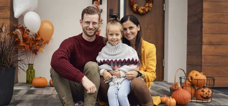 Family sits on a front porch in October with pumpkins around them.