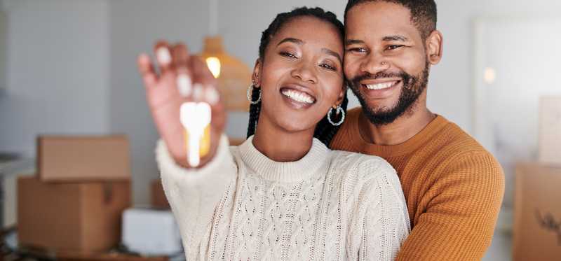 Two people smiling and holding a house key in a home with boxes.