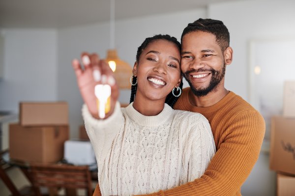 Two people smiling and holding a house key in a house with boxes.