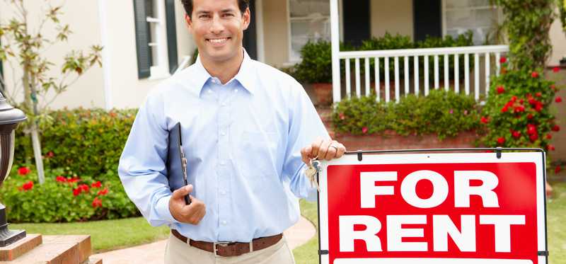 Person standing in front of For Rent sign in front of house.