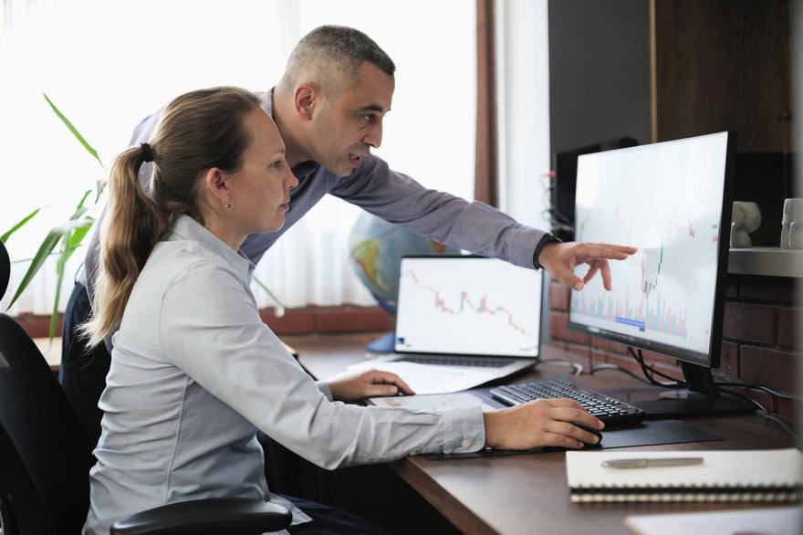 Two people looking at a computer monitor with a price chart.
