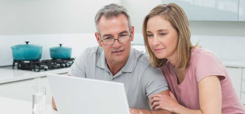 Two people looking at laptop in kitchen.