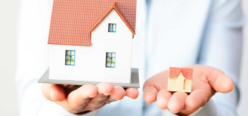Person holding their hands out with a miniature model home in one palm and a slightly larger one in the other.