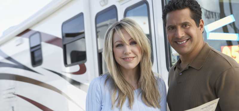 People smiling in front of a class A motor home and holding a magazine.