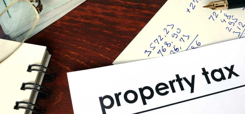 Document that says Property Tax lying next to a stack of money and calculations.