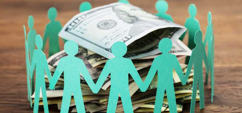 Green paper cut-outs of people holding hands around a pile of money.