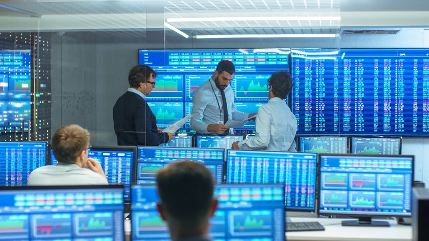 Stock traders discussing charts and surrounded by displays of market data.