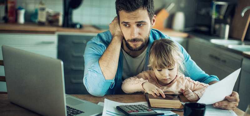 Worried person looking at laptop at kitchen table with child in their lap.