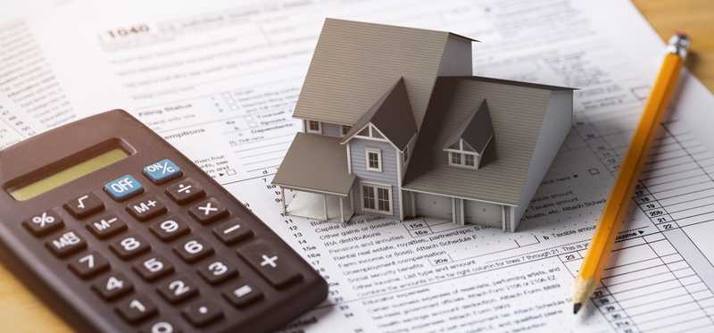 Miniature model home and a calculator sitting on top of tax forms.