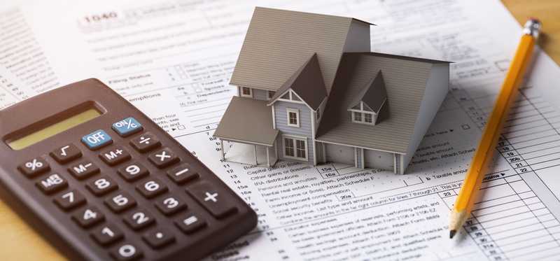 Miniature model house on top of tax forms with calculator and pencil.