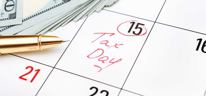 Tax Day written on the fifteenth day on a calendar with money and a pen beside it