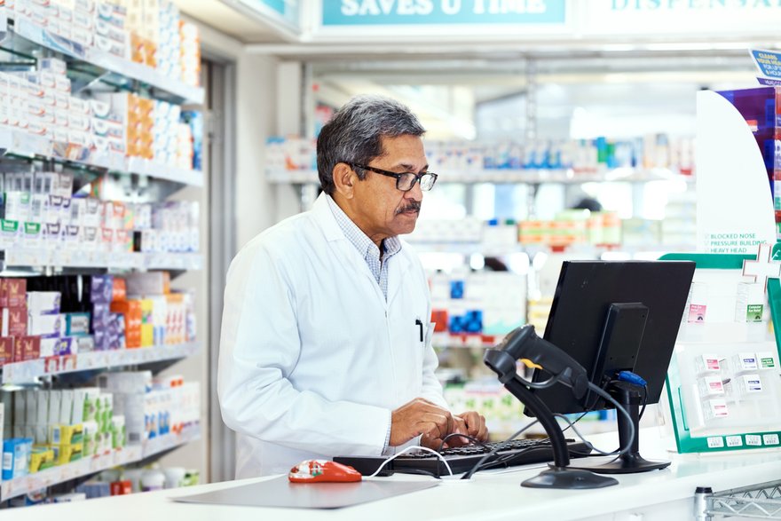 A pharmacist standing in front of medications and using a computer.
