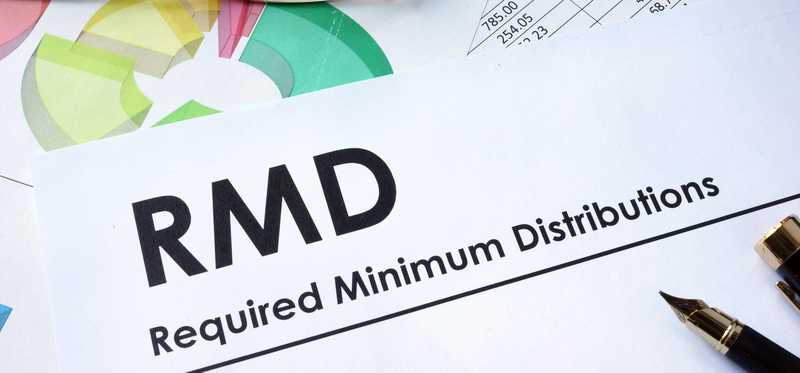 The words RMD Required Minimum Distributions on paper near a pen and a pair of glasses.