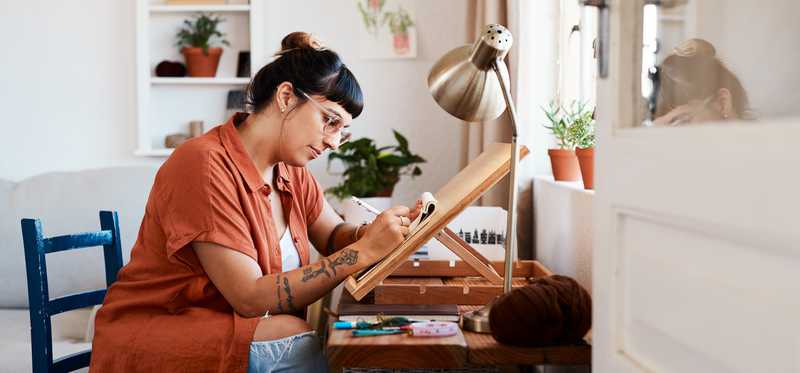 An artist is working at an easel while seated.