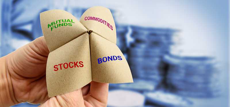 Hands playing a child's game with a folded paper labeled Stocks, Bonds, Commodities, and Mutual Funds.