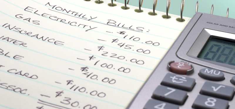 Part of a household budget written on paper next to a calculator.