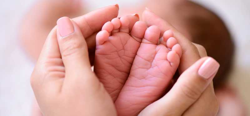 We see two adult hands cupping two tiny baby feet.