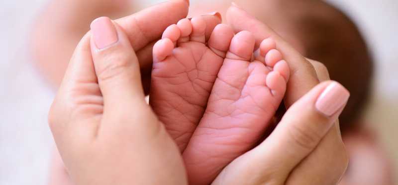 Two adult hands cupping two tiny baby feet.