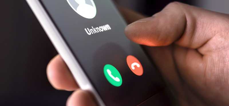 A handholding a phone that's receiving a call from an unknown caller.