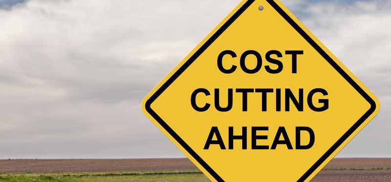 A yellow road sign says Cost Cutting Ahead.