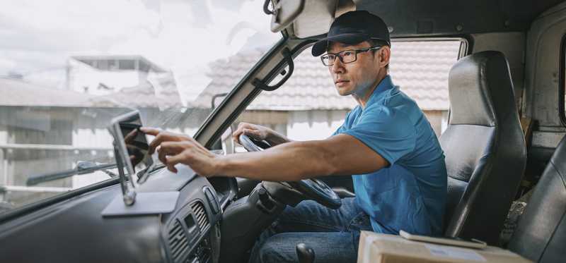 A driver is in a truck next to a box to be delivered.