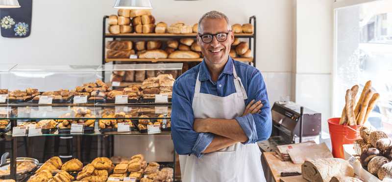A person in an apron is looking satisfied, with arms crossed, in a bakery.