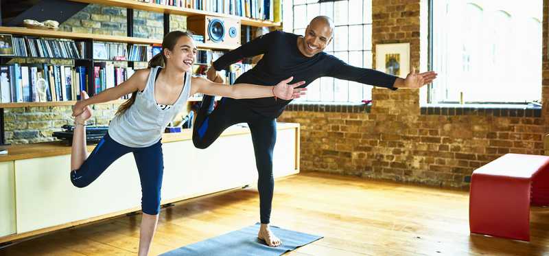 An adult and child are each balancing on one leg on a yoga mat.