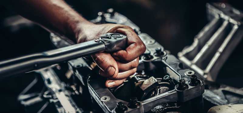 A hand is shown working on a car engine.