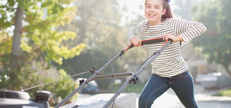 A girl is happily mowing a lawn.