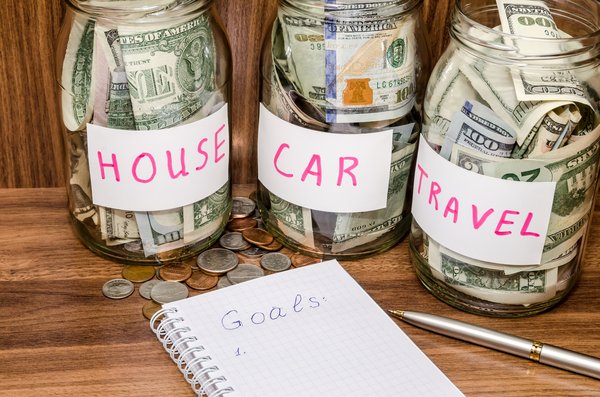 Three savings jars full of cash and labeled House, Car, and Travel.