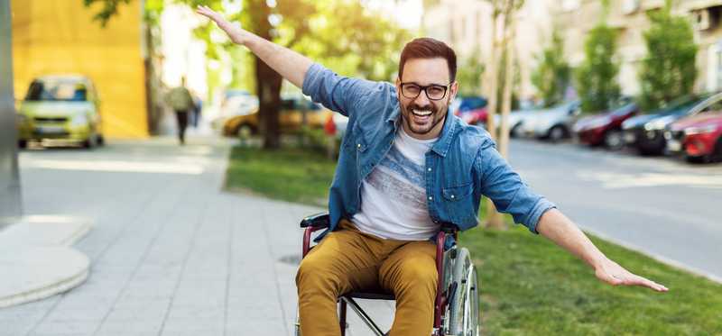 Person is outdoors, happy and smiling with arms outstretched.