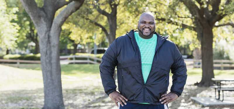 A person smiling and standing in a park.
