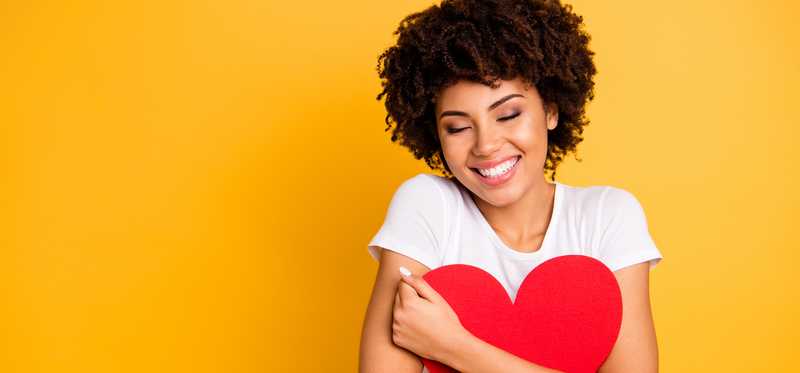 Someone is hugging a red heart cutout and smiling.