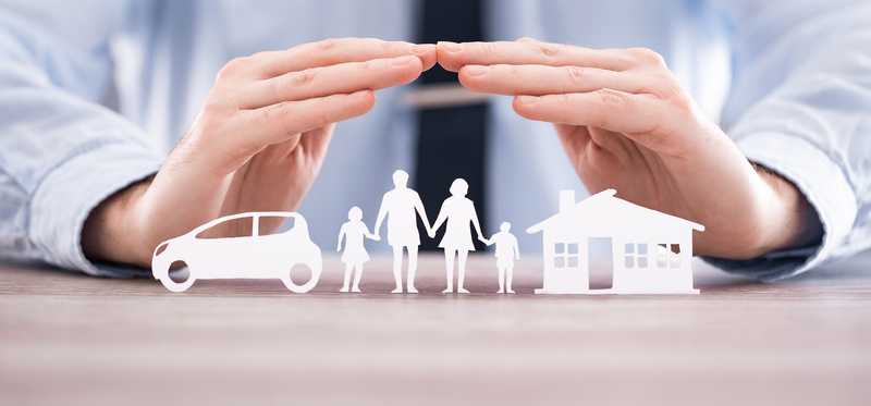 Two hands hovering over paper cutouts of a home, car, and family.