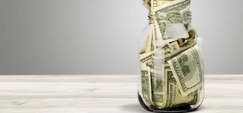 We see a glass jar stuffed full of cash, with hundred dollar bills visible.