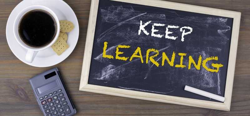 We see a small blackboard on which is written keep learning, next to a calculator, a cup of coffee, and some cookies.