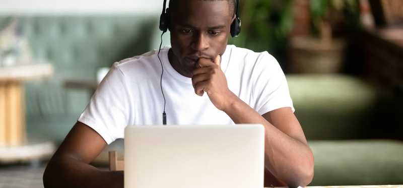 Person at a laptop is wearing headphones and looking deep in thought.