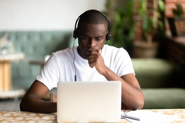 Person at a laptop is wearing headphones and looking deep in thought.