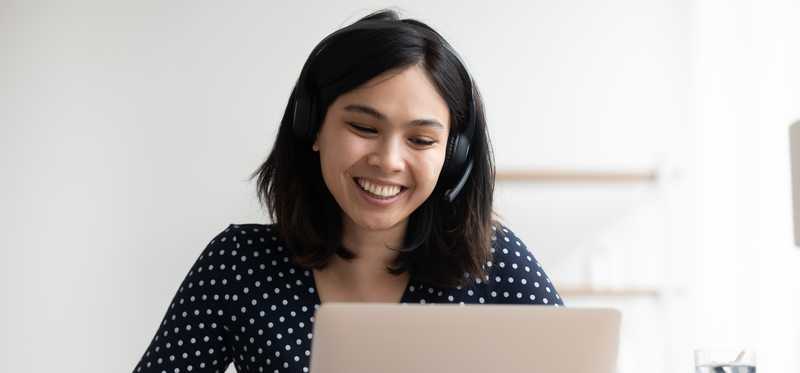 Person wearing headphones and smiling while looking at laptop.