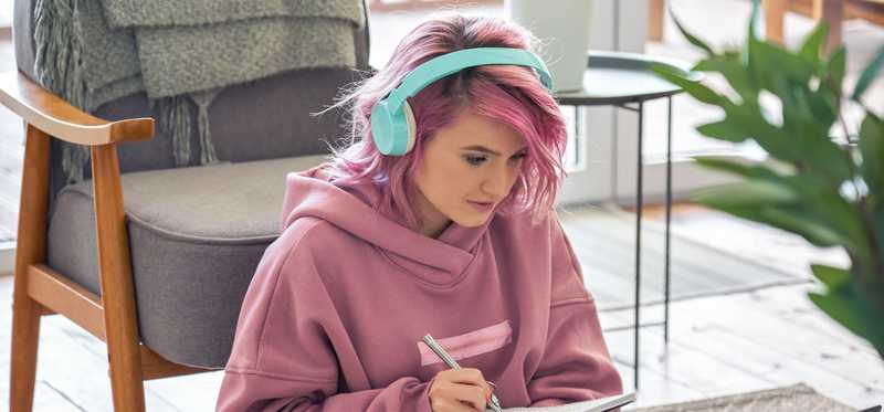 Person in headphones is looking at laptop and writing notes.