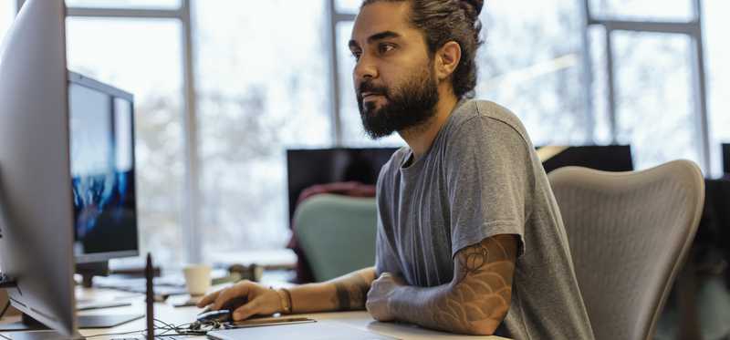 A person with a beard and tattoos working at a computer.