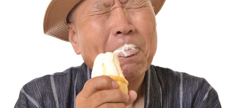 A man in a hat squinting and eating an ice cream cone