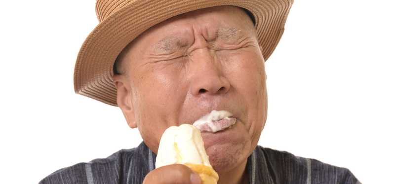 A person in a hat is squinting and eating an ice cream cone.