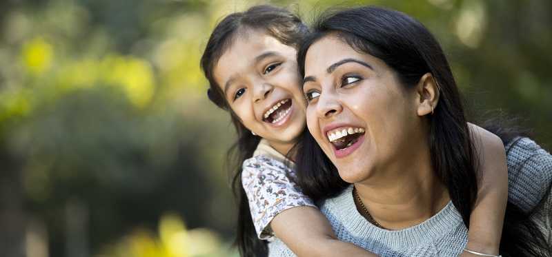 An adult has a child on their back and both are smiling.