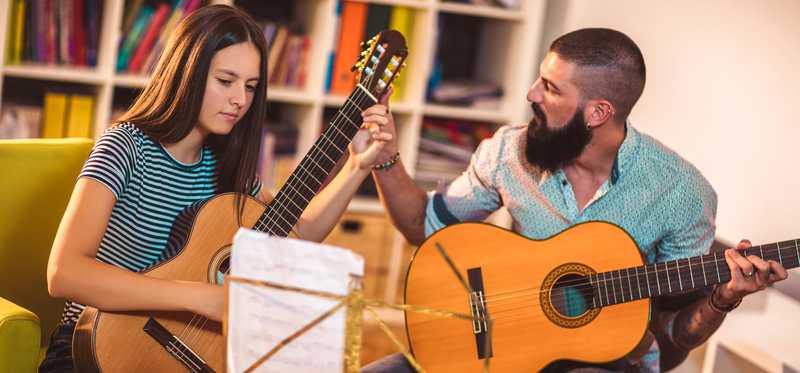 Adult teaching student how to play guitar.